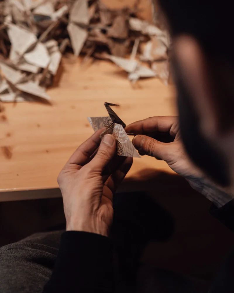 Manos plegando una pieza de papel sobre una mesa de trabajo con recortes ya plegados al fondo