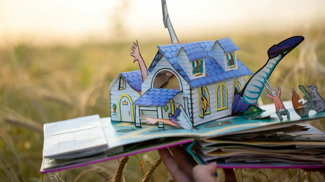 Libro desplegable abierto con una casa de papel levantada mediante construcción en V y varias figuras recortadas